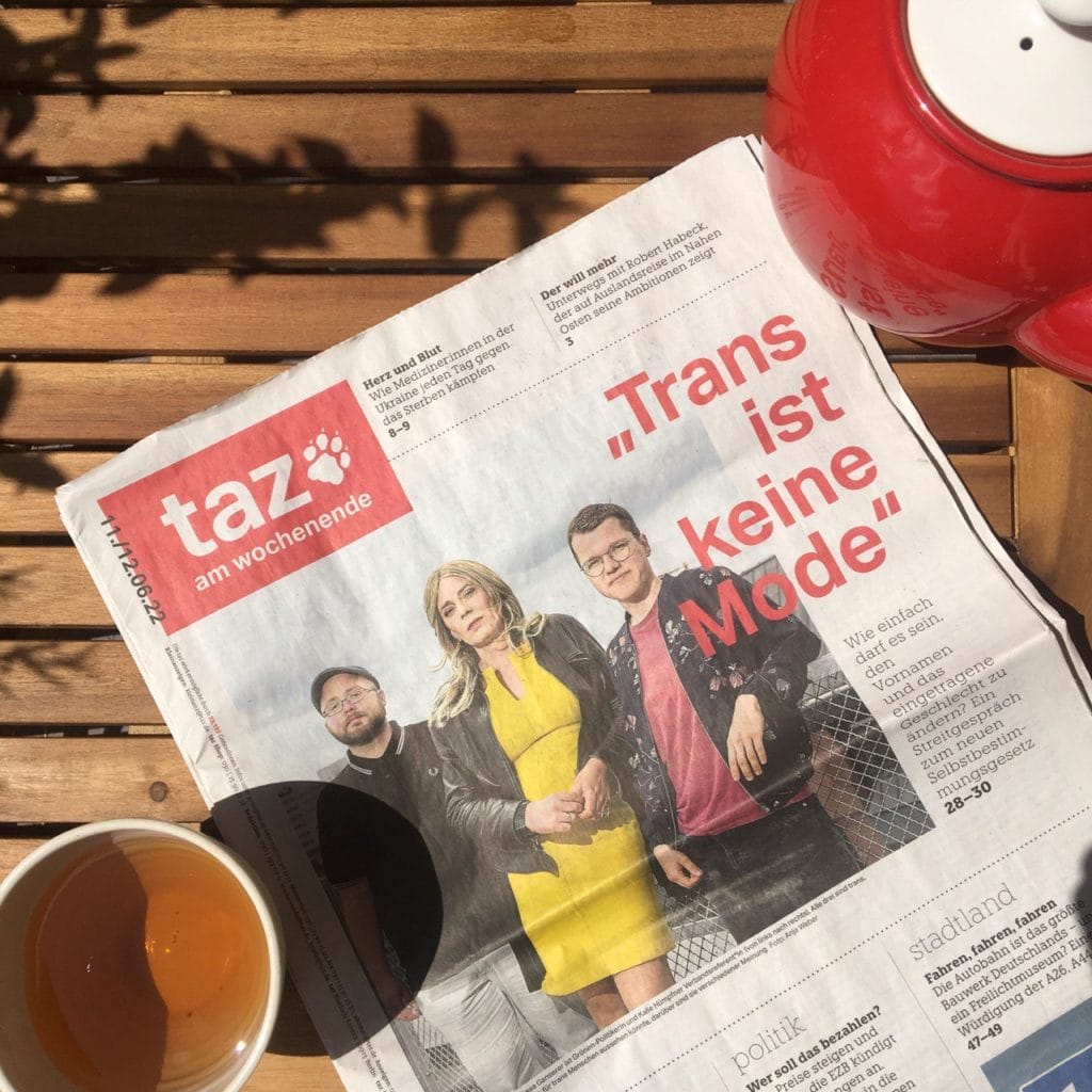 Titelseite der taz am Wochenende. Schlagzeile ist "Trans ist keine Mode" Daneben zu sehen von rechts nach links: Kalle vom BVT*, Tessa Ganserer und Till Amelung. 
